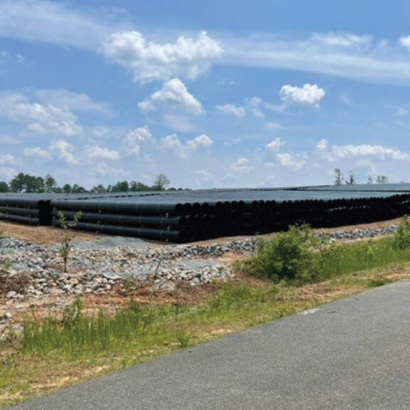 Stacked and organized black HDPE corrugated pipe on large job site.