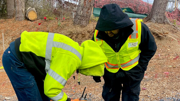 Two utility workers in yellow vests installing leak detection technology.