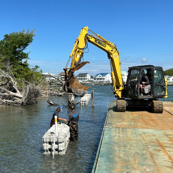 Excavator on platform in water installing shoreline protection structures